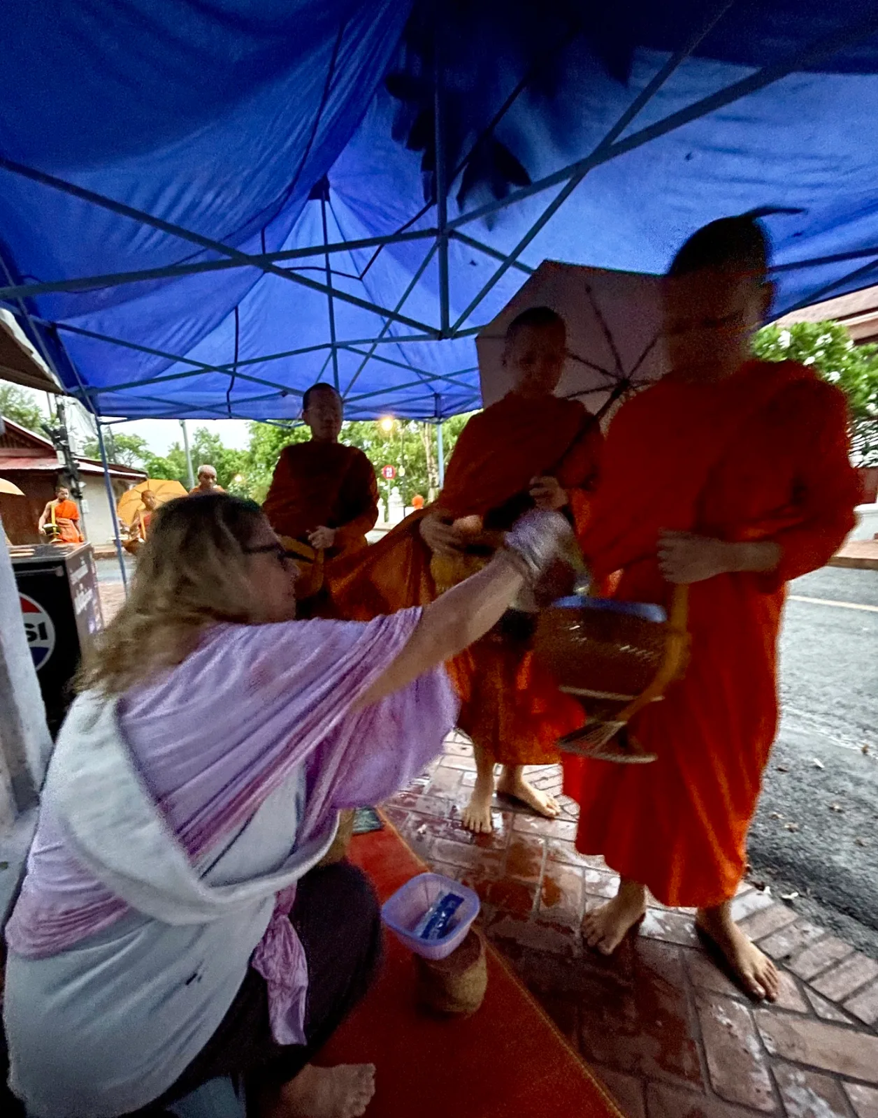A woman handing out rice to a monk in a saffron robe at the Tak Bat ceremony in Luang Prabang Laos