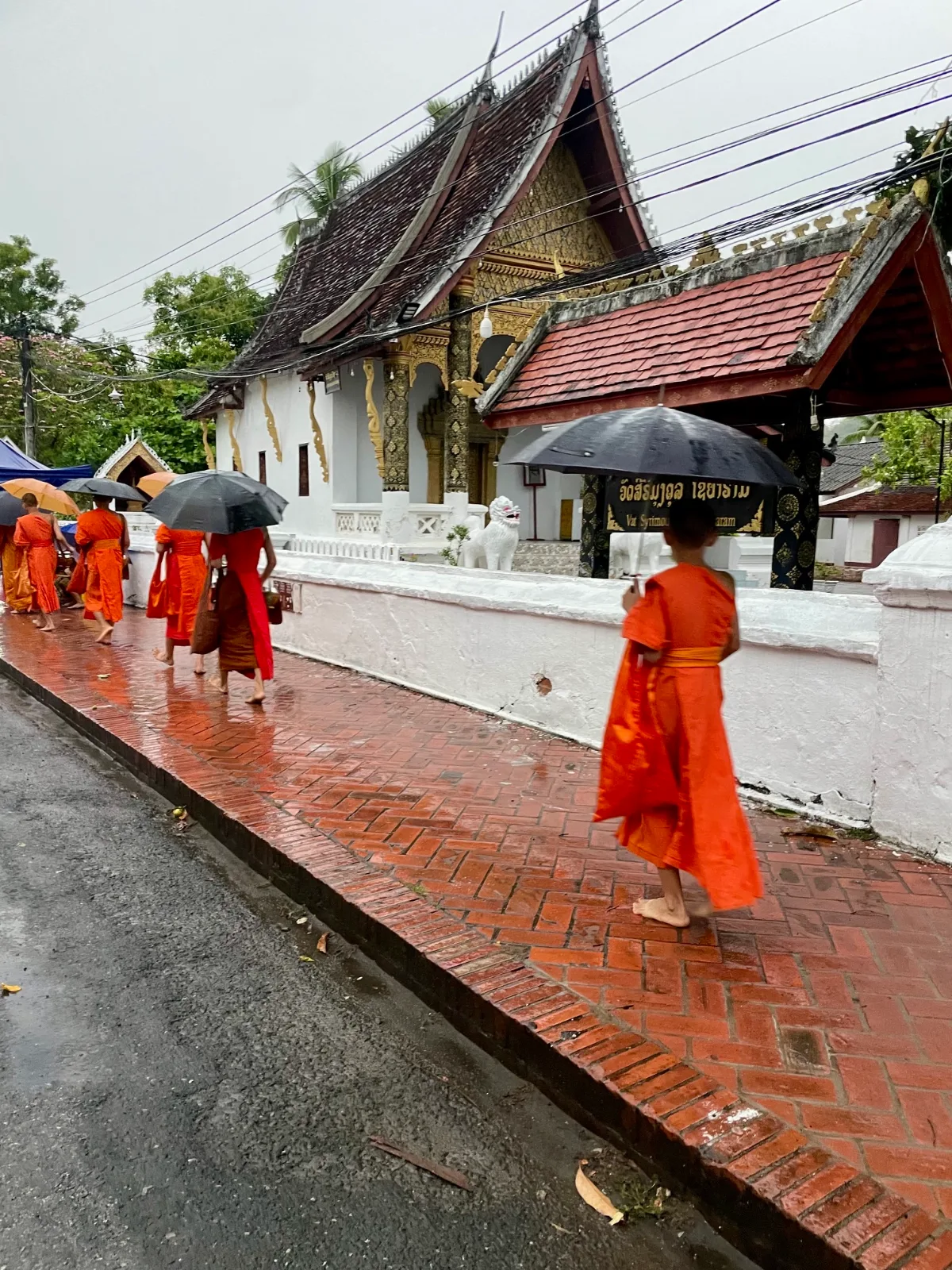 Monks in orange robes with umbrellas walking in front of a Buddhist temple in Laos