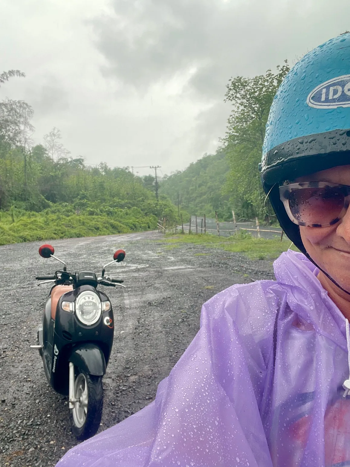 A woman with a purple rain poncho standing beside a motor scooter in Laos