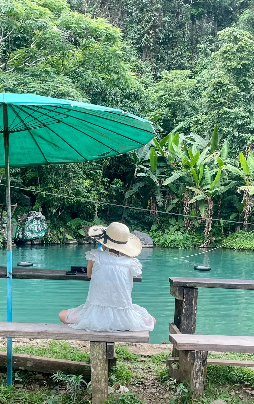 A woman in a white dress and a sun hat in front of one of the blue lagoons outside of Vang Vieng Laos