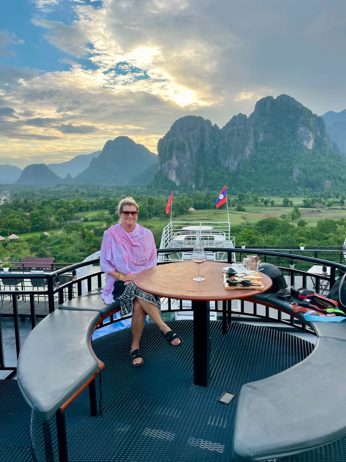 A woman sitting at a rooftop bar in Laos at sunset with mountains in the background